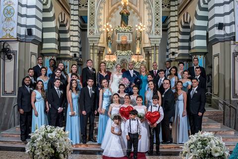 noivos posam junto aos padrinhos madrinhas pajens e damas de honra igreja altar balões de coração flores brancas'