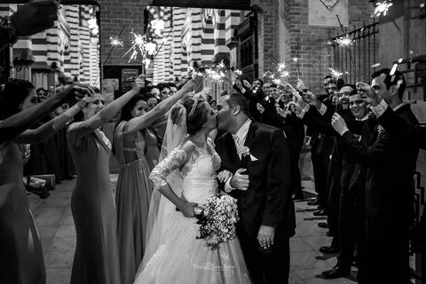 beijo dos noivos entre padrinhos que estendem bastões luminosos preto e branco'