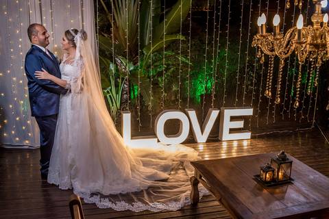 noivos se abraçam ao lado de letreiro luminoso decoração madeira lustre'