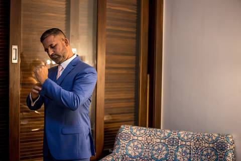 noivo se prepara para o casamento abotoa terno azul '