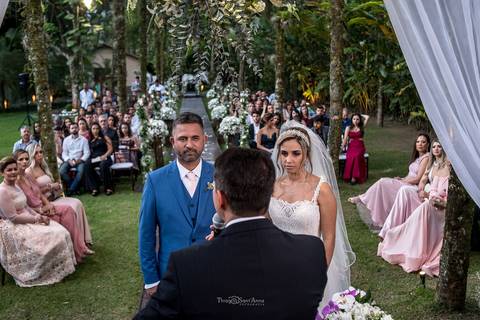 noivos no altar ambiente externo vegetação coqueiros flores brancas madrinhas convidados observam'
