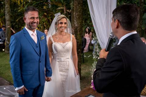 noivos sorrindo no altar junto ao pastor convidados ao fundo'