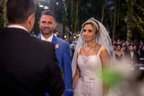noivos no altar observam o pastor convidados ao fundo '