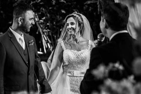 noivos sorrindo ao se olhar enquanto ouvem o pastor no altar'