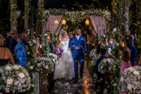 saída dos noivos noiva vestido véu buque em tons de rosa decoração vegetação flores brancas convidados observam de pé'