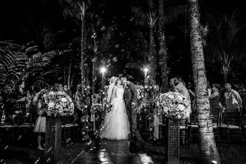 beijo dos noivos saída dos noivos noiva vestido véu buque em tons de rosa decoração vegetação flores brancas convidados observam de pé preto e branco'