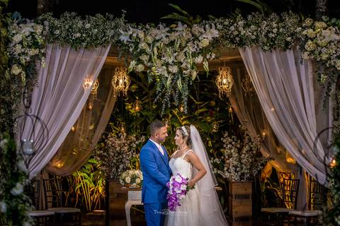 noivos abraçados noiva vestido véu noivo terno azul decoração estrutura madeira tecido branco flores brancas luminárias'