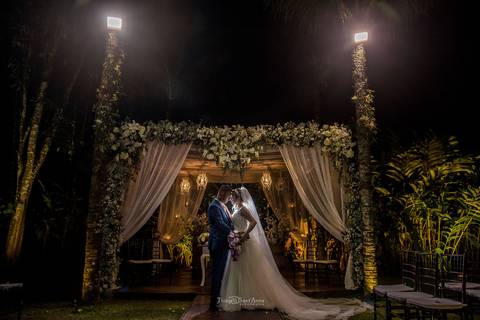 noivos abraçados noiva vestido véu noivo terno azul decoração estrutura madeira tecido branco flores brancas luminárias'