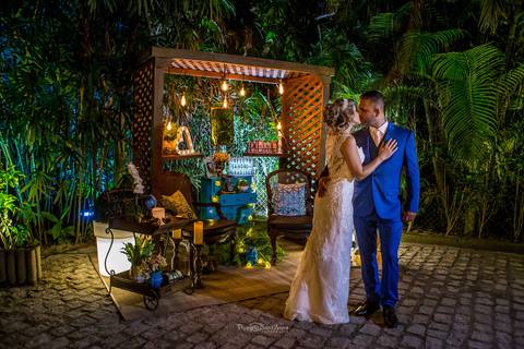 beijo dos noivos ambiente externo vegetação estrutura de madeira móvel almofadas azul celeste'