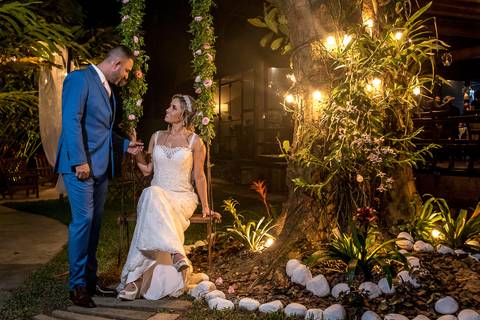 noiva sentada em balanço observa o noivo ao lado de uma árvore decorada'