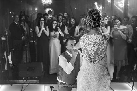 dança dos noivos pista noivo ajoelhado beija mão da noiva convidados observam preto e branco'