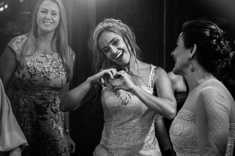 noiva faz gesto de coração com as mãos dançando com convidadas preto e branco'