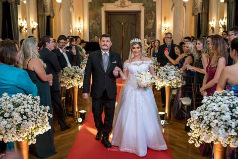 entrada da noiva e seu pai igreja  convidados observam de pé decoração flores brancas tapete vermelho'