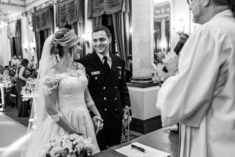 noivos sorrindo se observam frente ao padre igreja preto e branco'