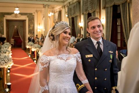 noivos sorrindo atentos ao padre tapete vermelho decoração flores brancas'