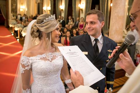 noivos sorrindo se observam padre lê documento ao microfone'