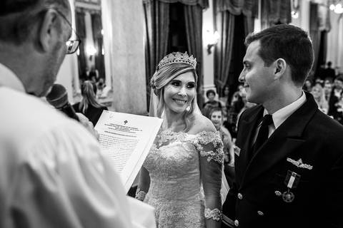 noivos sorrindo se observam padre lê documento ao microfone preto e branco'