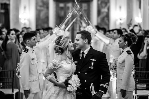 beijo dos noivos ao fundo militares de farda branca erguem espadas preto e branco '