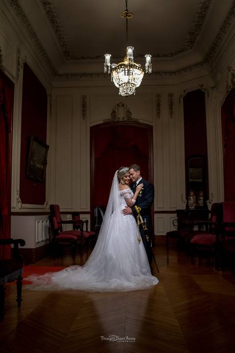 noivos se abraçam noiva vestido véu buque noivo farda militar espada'