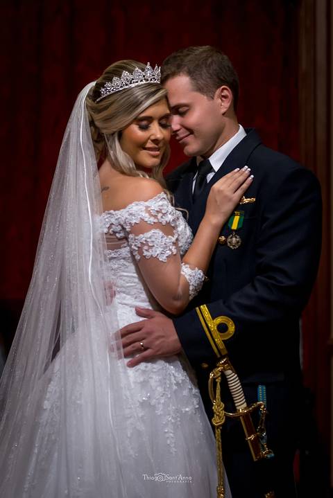 noivos se abraçam noiva vestido véu buque noivo farda militar espada'
