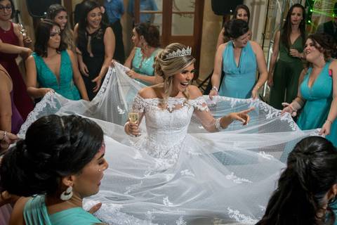 noiva sorri madrinhas em volta seguram barra de seu vestido'