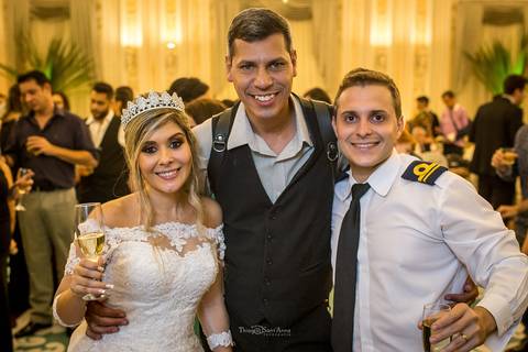 noivos posam sorrindo junto a fotógrafo  Thiago Sant'Anna convidados ao fundo'