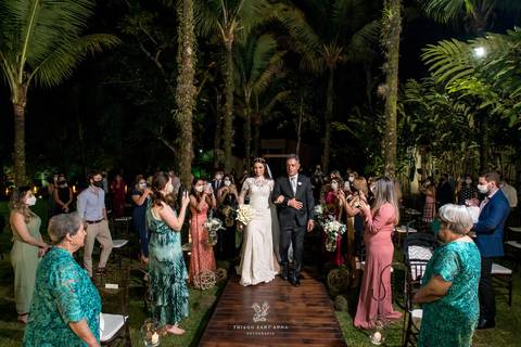 entrada da noiva com seu pai externo vegetação gramado palmeiras convidados observam de pé'