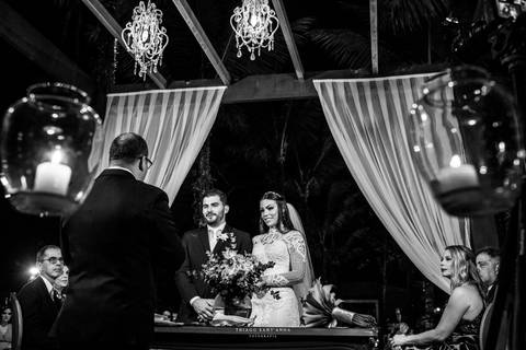 noivos atentos a cerimônia no altar frente ao pastor decoração velas cortinas brancas lustres'