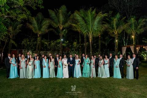 noivos posam com madrinhas vestido azul padrinhos terno preto ambiente externo gramada coqueiros'