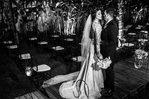 noivos posam altar ao fundo ambiente externo vegetação gramado coqueiros preto e branco'