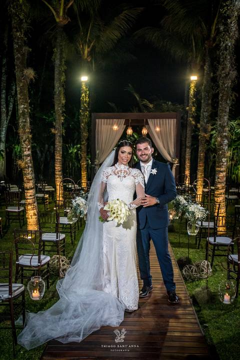 noivos posam altar ao fundo ambiente externo vegetação gramado coqueiros '