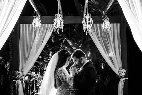 noivos posam abraçados noiva vestido véu noivo terno azul vegetação velas ao fundo '