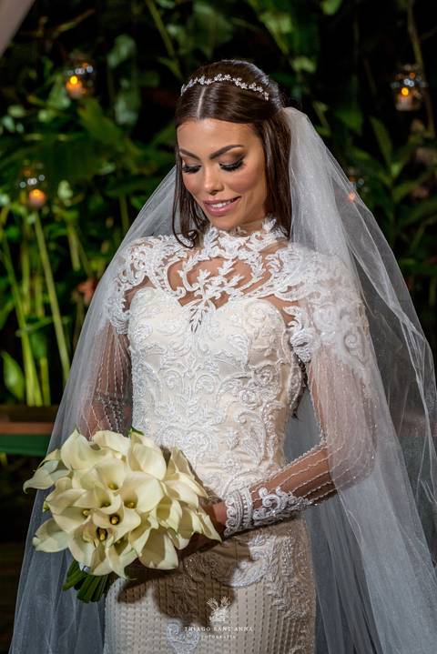 noiva sorri vestido renda véu buque copo de leite vegetação ao fundo'