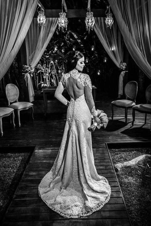 noiva sorri vestido renda véu buque copo de leite vegetação ao fundo preto e branco'