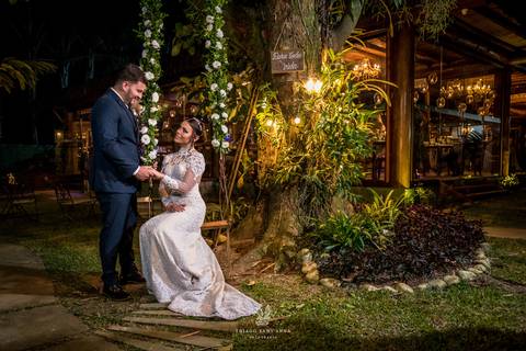 noiva sentada em balanço decorado com flores segura mão do noivo árvore iluminada jardim'