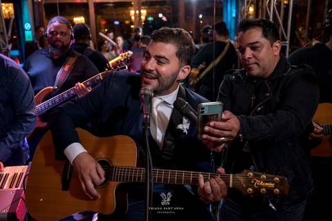noivo toca violão e canta junto a banda no palco'