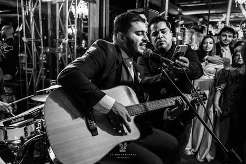 noivo toca violão e canta junto a banda no palco preto e branco'