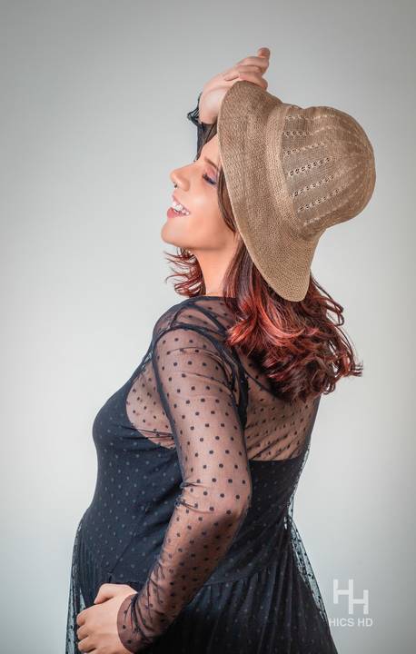 ensaio indoor ensaio interno em Brasília ensaio de gestante com chapéu no fundo branco ensaio em estúdio Brasília ensaio de gravidez foto de gestante em fundo branco rindo de lado para a câmera em Brasília '