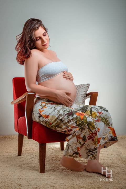ensaio indoor ensaio interno em Brasília ensaio de gestante sentada em poltrona acariciando a barriga ensaio de gravidez  foto de gestante em estúdio em Brasília'