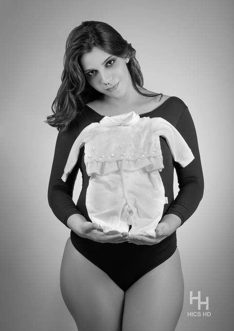 ensaio indoor ensaio interno em Brasília ensaio de gestante no fundo preto e branco ensaio em estúdio Brasília ensaio de gravidez foto de gestante em preto e branco posando de maiô ensaio de gravidez Brasília segurando roupa de bebê'