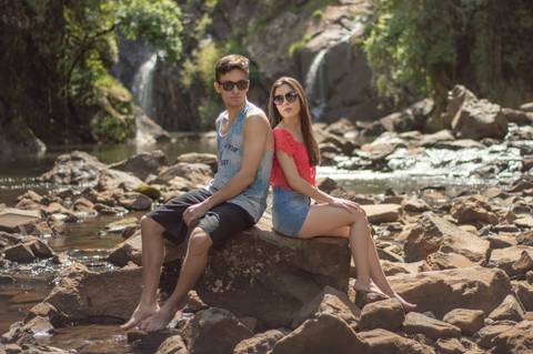 ensaio de casal da brenda e do sergio em um dia ensolarado nas ruas da cidade de ivoti nas casas eixamel fotografo de casal em sao leopoldo casal boeira sentados na pedra com cachoeira de fundo'