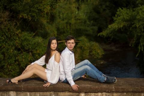 ensaio de casal da brenda e do sergio em um dia ensolarado nas ruas da cidade de ivoti nas casas eixamel fotografo de casal em sao leopoldo casal boeira sentados na ponte com fundo verde'