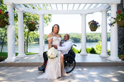 Photo by Vanessa Trettel,
Onsite wedding photographer at The Water View, Monroe, CT in July 2022.
It's an image of the bride standing with the bouquet and the groom behind sitting in the wheel chair with the river in the background'