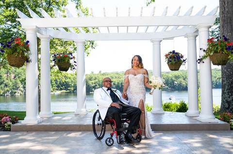 Photo by Vanessa Trettel,
Onsite wedding photographer at The Water View, Monroe, CT in July 2022.
It's an image of the bride standing with the bouquet and the groom behind sitting in the wheel chair with the river in the background'