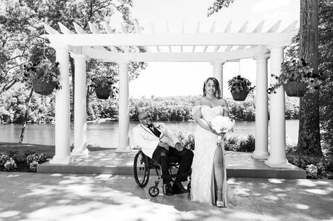 Photo by Vanessa Trettel,
Onsite wedding photographer at The Water View, Monroe, CT in July 2022.
It's an image of the bride standing with the bouquet and the groom behind sitting in the wheel chair with the river in the background'