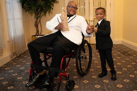 Photo by Vanessa Trettel,
Onsite wedding photographer at The Water View, Monroe, CT in July 2022.
It is an image of the boy standing holding the ring and the groom in his wheelchair.'