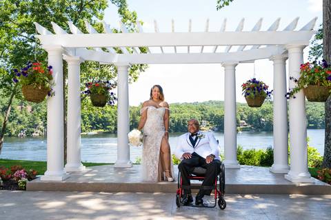 Photo by Vanessa Trettel,
Onsite wedding photographer at The Water View, Monroe, CT in July 2022.
It's an image of the bride standing with the bouquet and the groom behind sitting in the wheel chair with the river in the background'