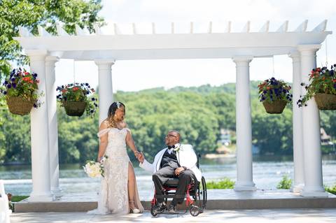Photo by Vanessa Trettel,
Onsite wedding photographer at The Water View, Monroe, CT in July 2022.
It's an image of the bride standing with the bouquet and the groom behind sitting in the wheel chair with the river in the background'