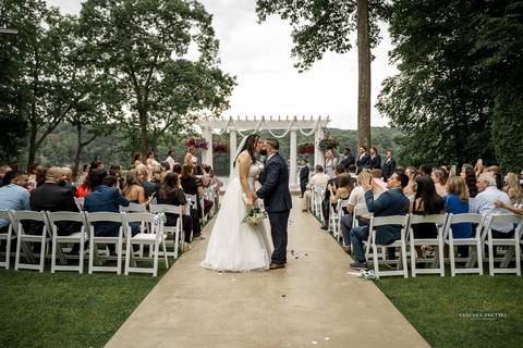 A lively wedding ceremony at The Waterview in Monroe, CT. A groomsman joyfully hands out beers to smiling guests, setting a fun and unique tone that perfectly matches the joyful personalities of Briana & Nicholas.'