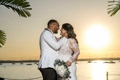 Captured in the soft glow of the setting sun, Jessica & Ben share a kiss at Anthony's Ocean View. The ocean and the vibrant sunset create a romantic atmosphere, making this moment feel truly magical.'